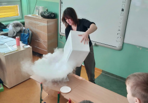 Nauczycielka wrzuca suchy lód do miski z ciepłą wodą.
