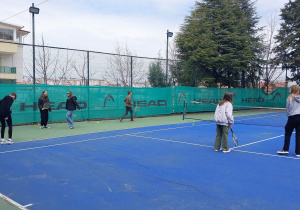 Uczniowie grają na korcie w tenisa ziemnego.