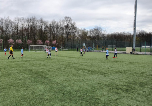 Uczniowie rozgrywają mecz piłki nożnej na murawie boiska.