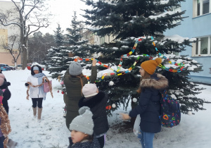 uczniowie dekorują choinkę przed blokiem