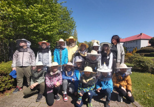 Grupowe zdjęcie uczestników wycieczki w strojach pszczelarza.
