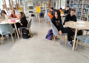 Uczniowie siedzący w grupach przy trzech stolikach uważnie przysłuchują się instrukcjom do zadania