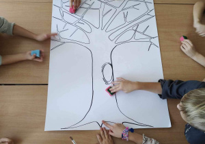 Uczniowie malują drzewo przy użyciu gąbek maczanych w farbach.