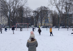 Uczniowie na boisku szkolnym rzucają się śnieżkami.