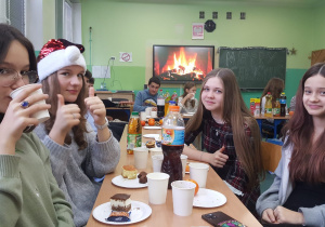 nasi najstarsi uczniowie siedzą w klasie przy stole zastawionym różnymi smakołykami, w tle rozpalony kominek z yt