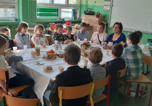uczniowie klasy 3a z katechetką siedzą przy stole zastawionym smakołykami