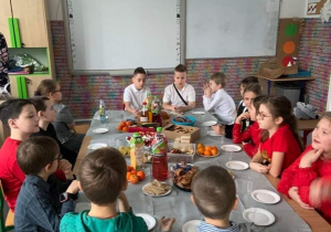uczniowie klasy 3b siedzą przy stole zastawionym różnymi smakołykam